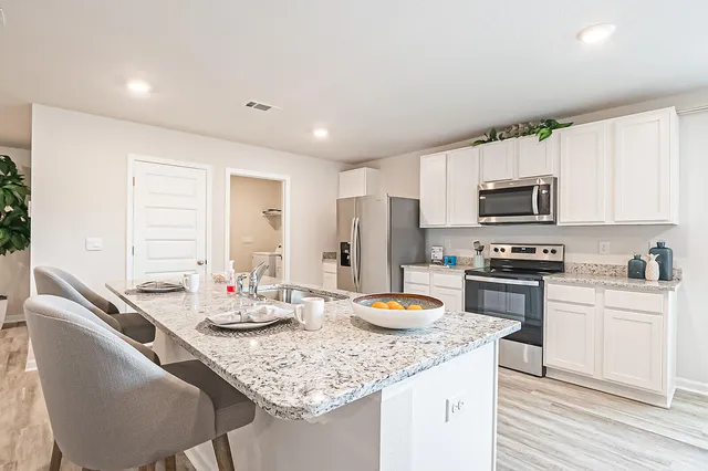 a kitchen with stainless steel appliances granite countertop a sink dishwasher a stove a refrigerator with a dining table and chairs