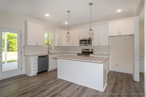 a kitchen with stainless steel appliances granite countertop a sink a stove a refrigerator and white cabinets with wooden floor