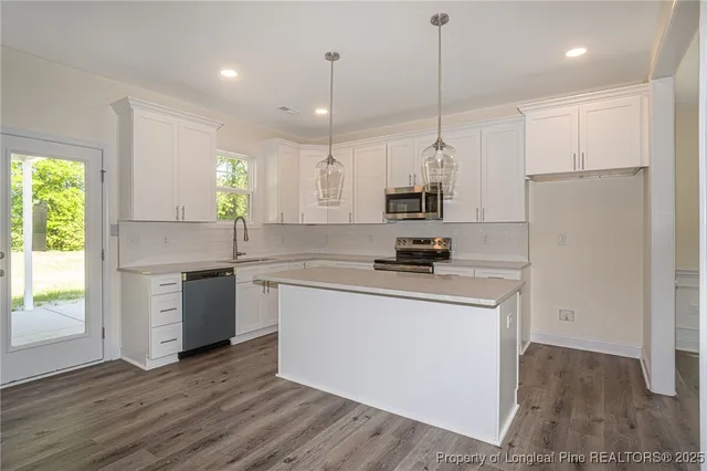 a kitchen with stainless steel appliances granite countertop a sink a stove a refrigerator and white cabinets with wooden floor