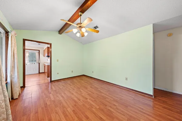 an empty room with wooden floor chandelier fan and windows