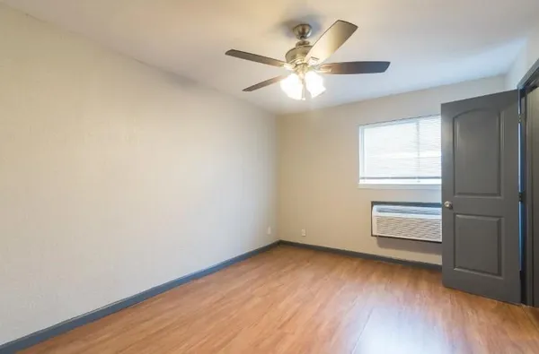 an empty room with wooden floor fan and windows