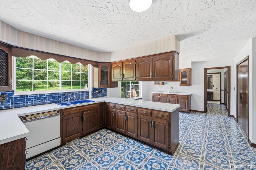 7020 Rattalee Lake Road Clarkston, MI 48348 - Photo 15 of 47 Kitchen featuring wood cabinetry, white countertops, a blue tile backsplash, and patterned tile flooring