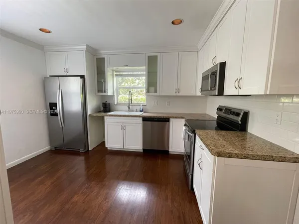 a kitchen with stainless steel appliances granite countertop a stove a sink dishwasher a refrigerator and white cabinets with wooden floor