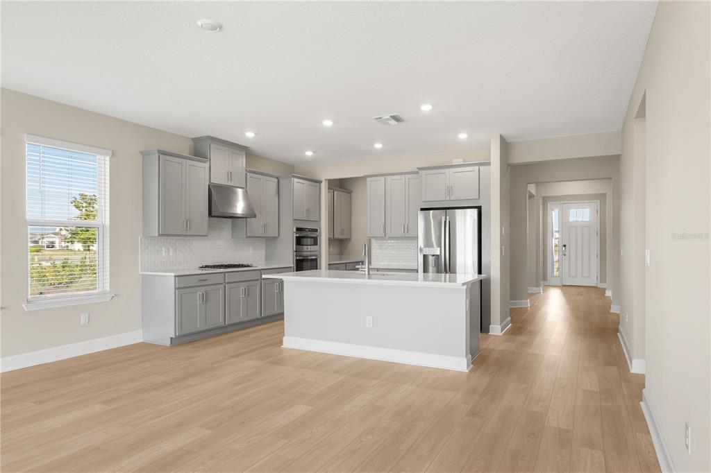 2181 Longliner Loop Wesley Chapel, FL 33543 - Photo 10 of 44 a large kitchen with kitchen island a sink wooden floor white stainless steel appliances and cabinets