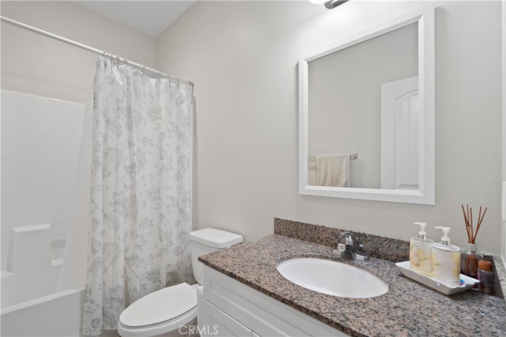 12875 Wainwright Lane Moreno Valley, CA 92555 - Photo 15 of 37 a bathroom with a granite countertop sink toilet a mirror a vanity and shower