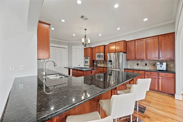 a kitchen with granite countertop a refrigerator oven a sink dishwasher and white cabinets with wooden floor