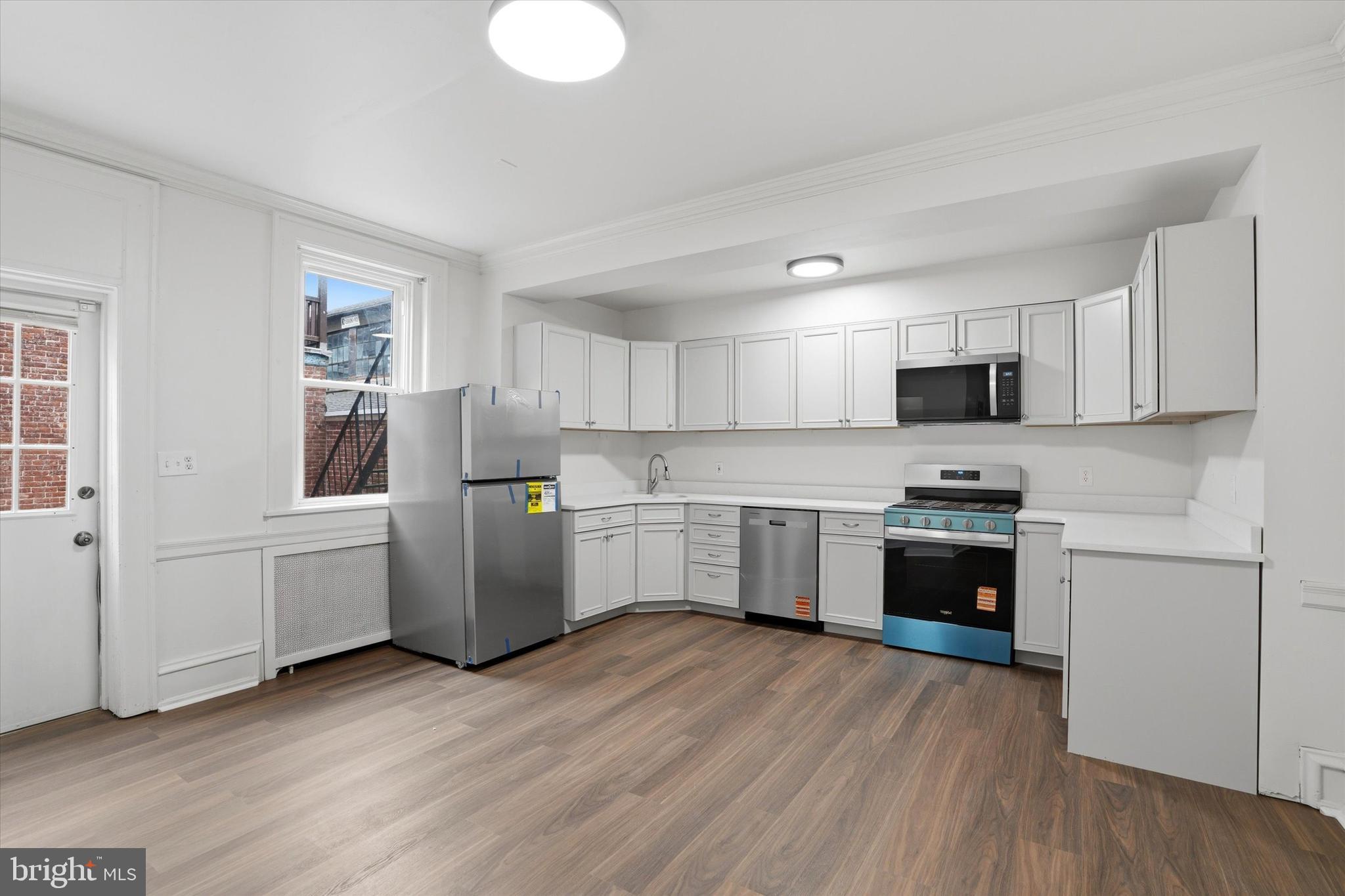 112 North 11th Street, Unit 1 Reading, PA 19601 - Photo 10 of 17 a kitchen with a refrigerator a stove top oven a sink dishwasher and white cabinets with wooden floor