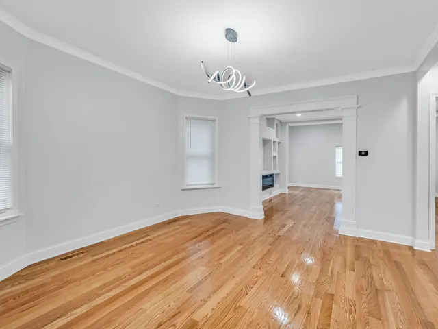 a big room with wooden floor a chandelier fan and windows