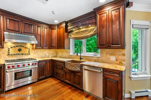 a kitchen with stainless steel appliances granite countertop a refrigerator a sink dishwasher a stove and a dining table with wooden floor