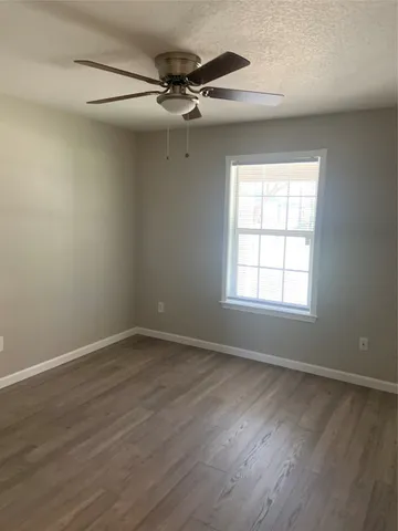 an empty room with wooden floor fan and windows