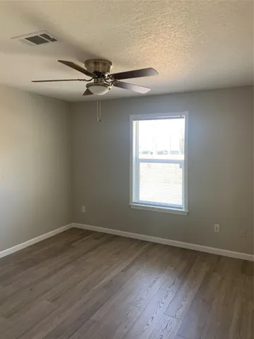 an empty room with wooden floor windows and fan