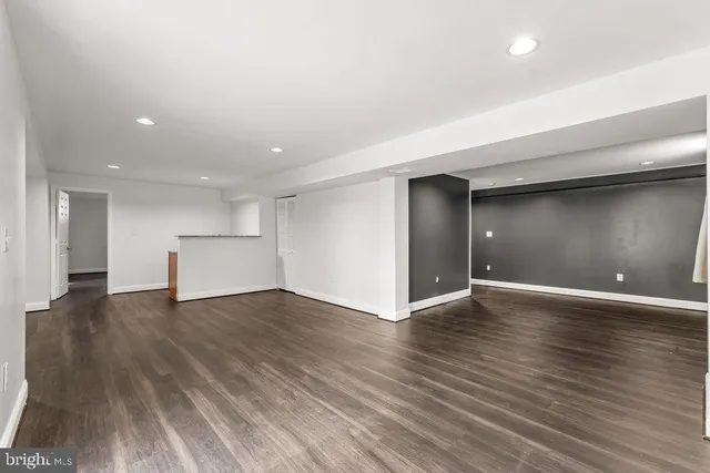 a view of an empty room with wooden floor and kitchen