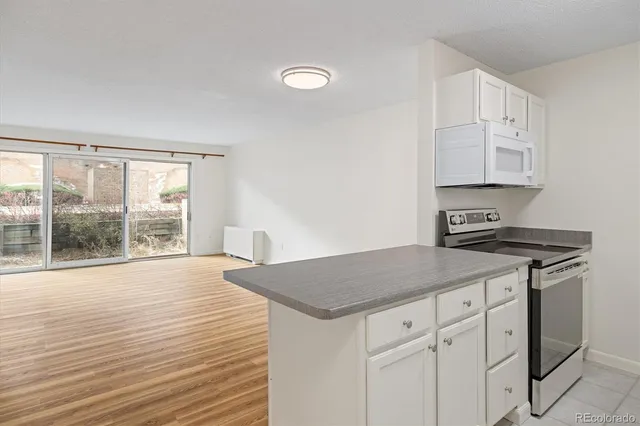 a kitchen with granite countertop a stove a sink and white cabinets with wooden floor