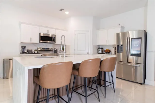 a kitchen with stainless steel appliances granite countertop a dining table chairs refrigerator and microwave