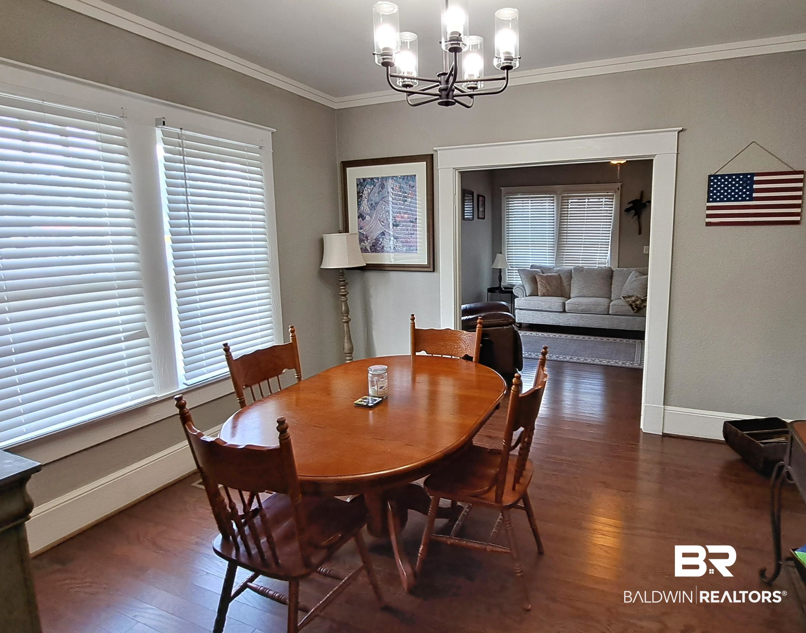 110 South Main Street Evergreen, AL 36401 - Photo 7 of 27 Dining area featuring wood-finish flooring, a contemporary chandelier, crown molding, and two large windows with horizontal blinds