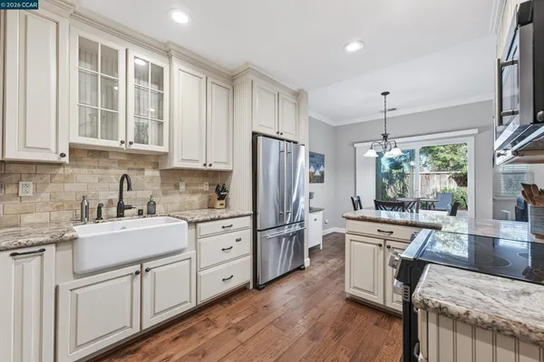 a kitchen with stainless steel appliances granite countertop a refrigerator a sink dishwasher a stove top oven a dining table and chairs with wooden floor