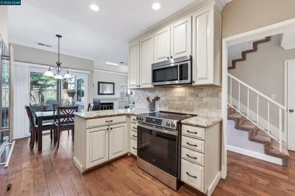 a kitchen with stainless steel appliances a stove a sink dishwasher a microwave oven and a dining table with wooden floor