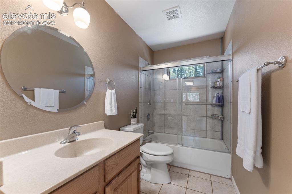 657 Spring Valley Drive Divide, CO 80814 - Photo 21 of 43 Bathroom featuring a wood-finish vanity with a built-in sink, a large oval mirror, and a shower-tub combination with sliding glass doors