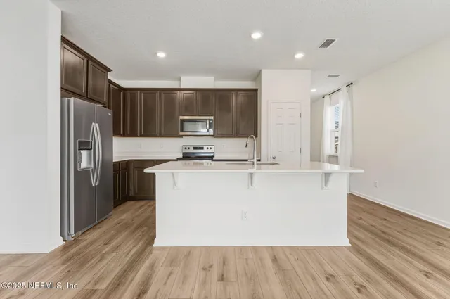 a large kitchen with stainless steel appliances a large counter top a stove a refrigerator a sink and a refrigerator