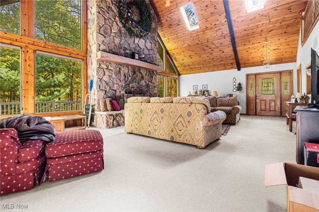 Carpeted living area with a skylight, high vaulted ceiling, wood ceiling, and a fireplace