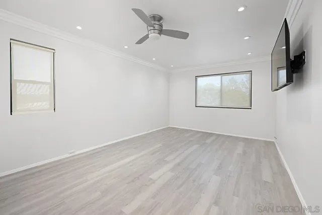 an empty room with wooden floor fan and windows