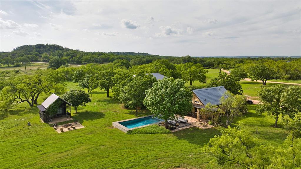 2969 County Lane Talpa, TX 76882 - Photo 10 of 40 Expansive property featuring a main residence with a metal roof, a rectangular swimming pool with an adjacent patio, and a separate structure with a covered porch and outdoor fire pit area
