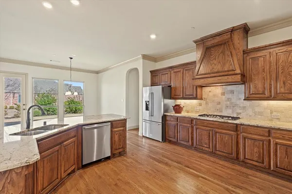 a kitchen with stainless steel appliances granite countertop a stove a sink dishwasher a refrigerator and wooden cabinets with wooden floor