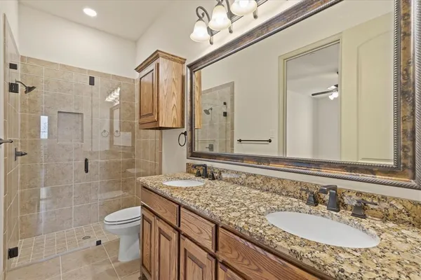 a bathroom with a granite countertop sink a toilet a mirror and shower