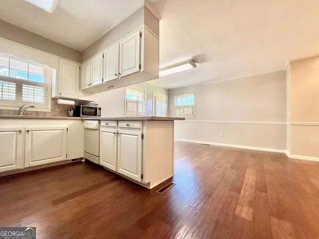 a living room with stainless steel appliances kitchen island granite countertop a refrigerator a stove a sink and dishwasher with wooden floor