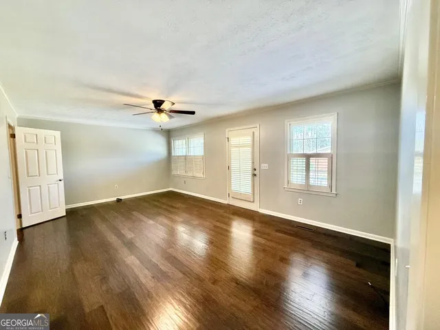 an empty room with wooden floor fan and windows