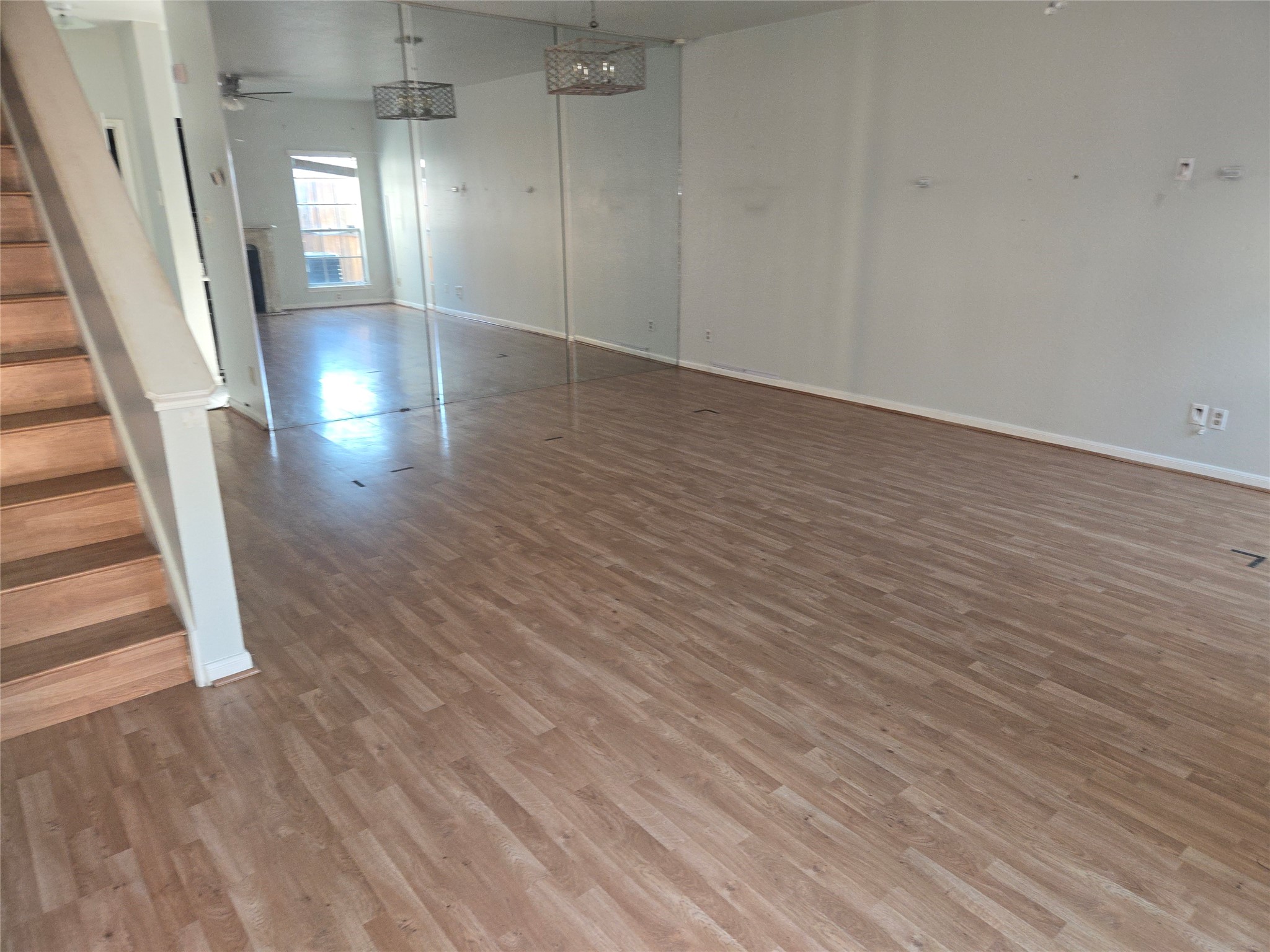 3780 Tanglewilde Street, Unit 501 Houston, TX 77063 - Photo 20 of 26 This spacious, open-plan living area features laminate wood flooring, neutral walls, and ample natural light. The room includes a staircase leading to an upper level and modern light fixtures, with a view extending to a windowed area at the back.