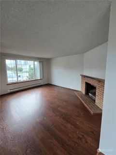 an empty room with wooden floor fireplace and windows
