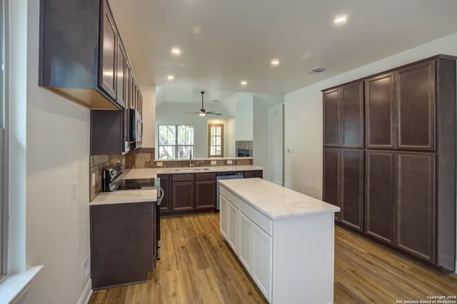 a kitchen with kitchen island granite countertop wooden floors stainless steel appliances a sink and a refrigerator