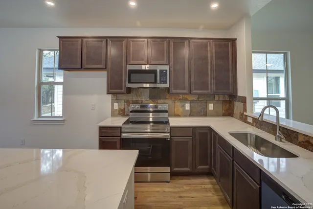 a kitchen with stainless steel appliances kitchen island granite countertop a sink dishwasher a stove and a refrigerator with wooden floor