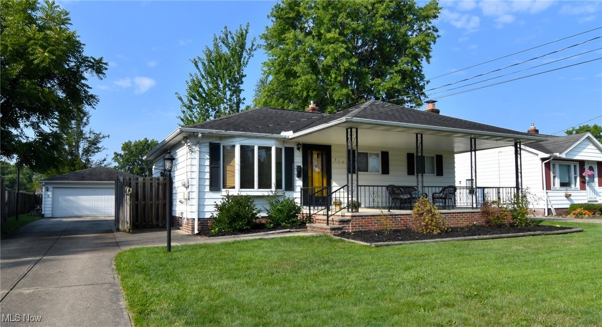 View of front of home featuring a garage, a front lawn, covered porch, and an outbuilding