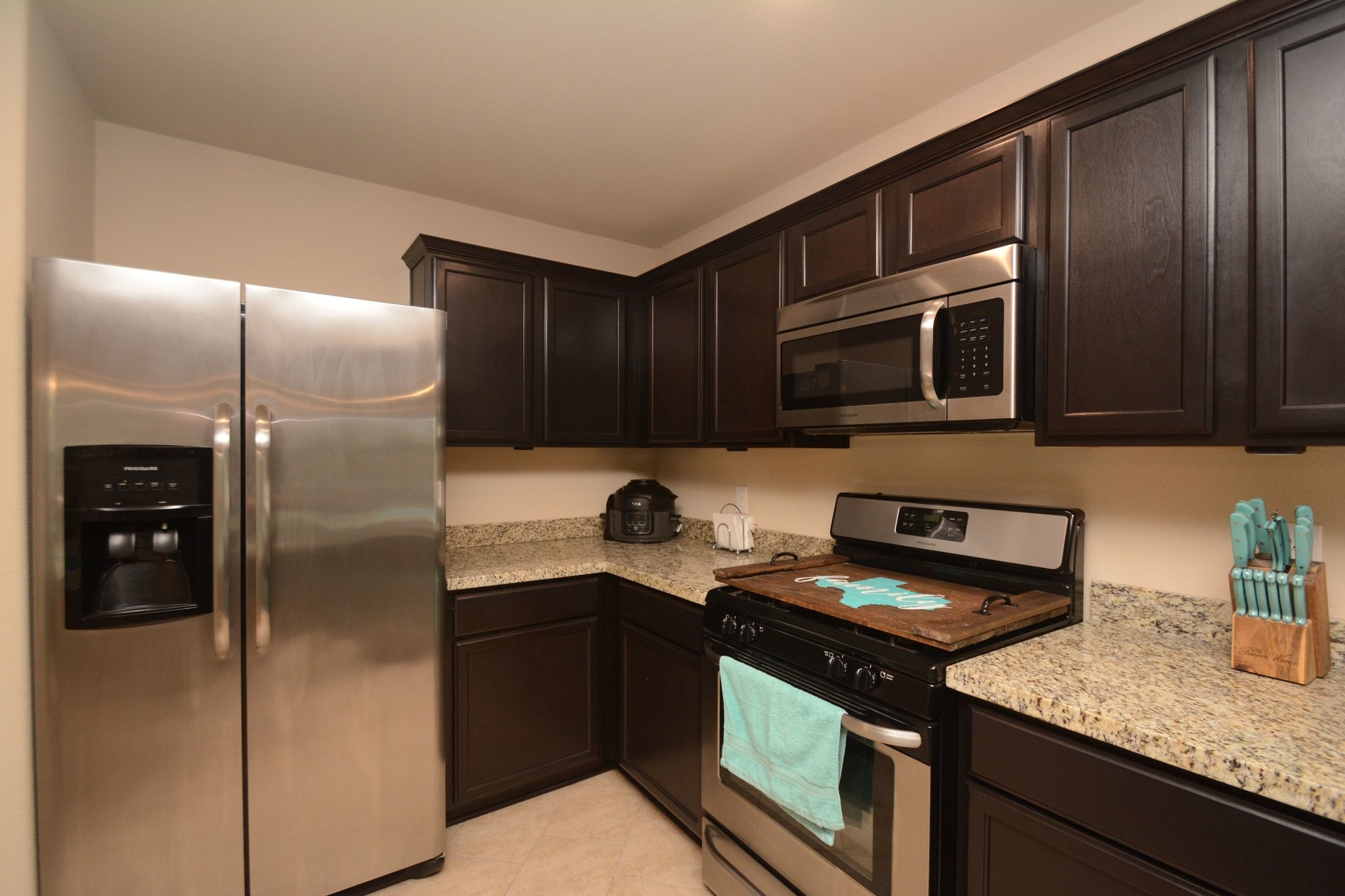 23318 Dukes Run Drive Spring, TX 77373 - Photo 11 of 41 This modern kitchen features dark wood cabinets, granite countertops, and stainless steel appliances, including a double-door fridge and a built-in microwave. It has a cozy, efficient layout with tiled flooring.