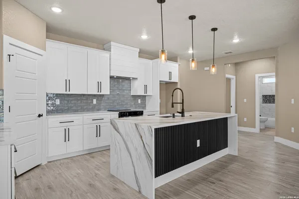 a kitchen with stainless steel appliances granite countertop a sink a stove a refrigerator and white cabinets with wooden floor