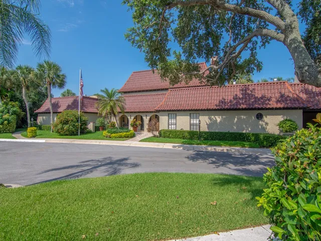 a sign board with flower plants and large trees