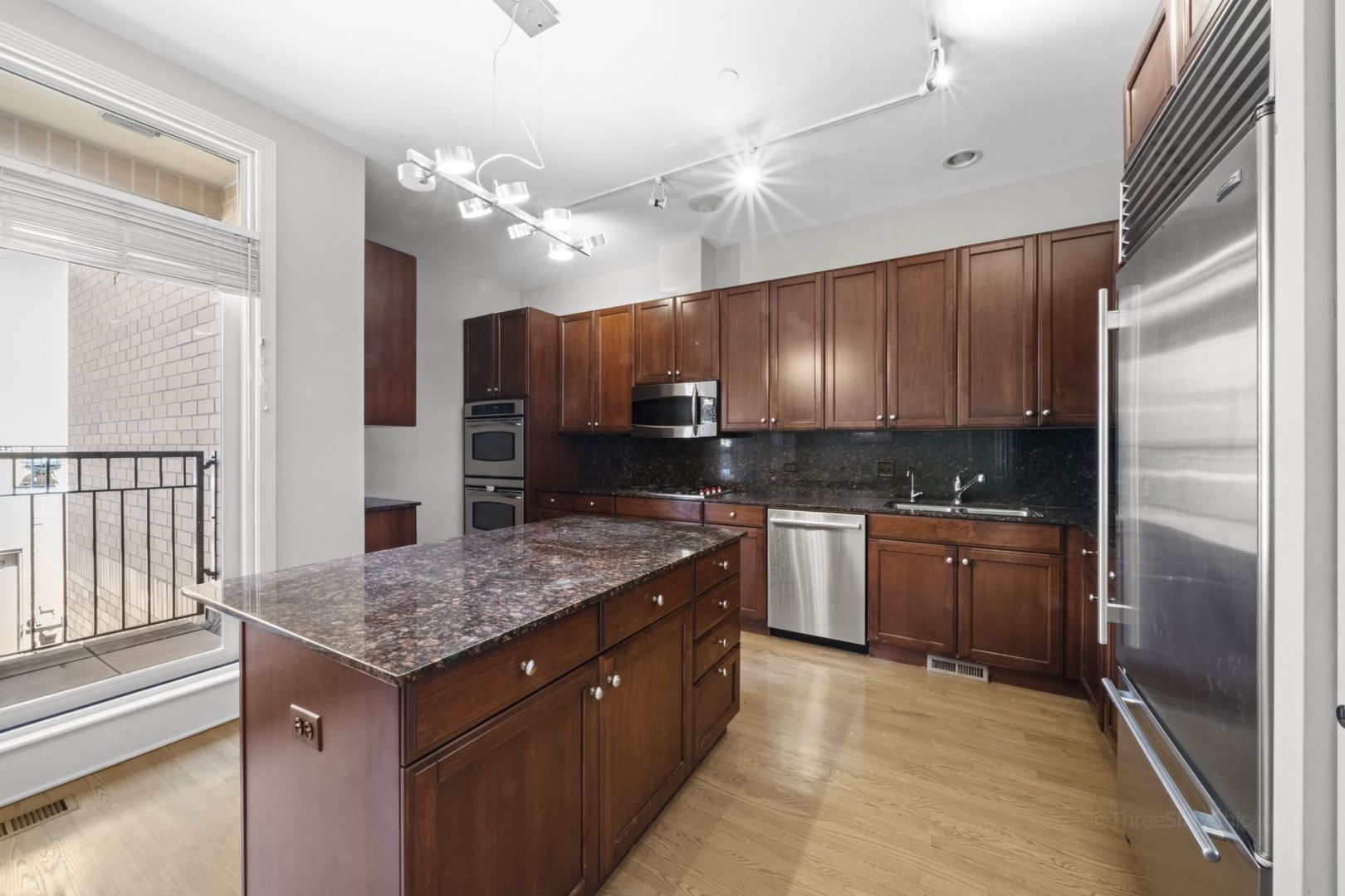 1137 West Monroe Street, Unit 17 Chicago, IL 60607 - Photo 9 of 41 a kitchen with kitchen island granite countertop wooden cabinets and a refrigerator