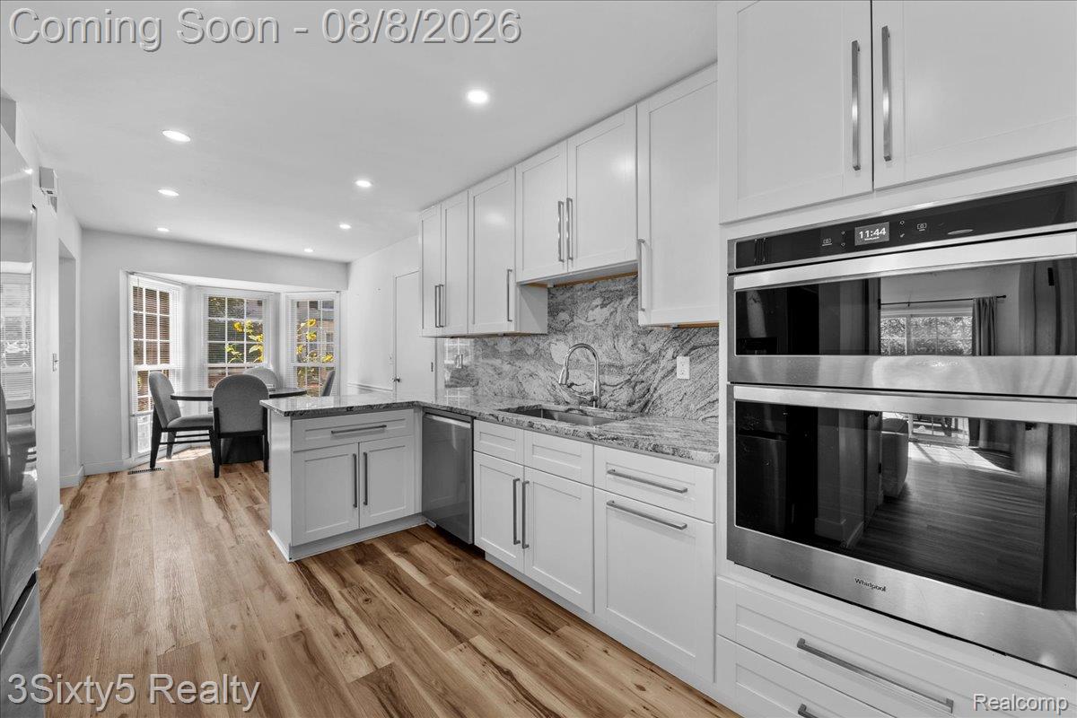 1189 Pine Ridge Court Rochester, MI 48306 - Photo 8 of 41 Sophisticated kitchen featuring white cabinetry with brushed metal hardware, marble-finish backsplash, wood-finish flooring, and stainless steel built-in appliances including double wall ovens and under-counter refrigeration