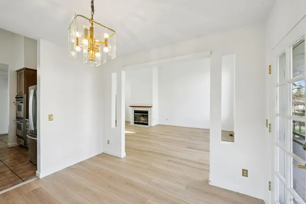 a view of an empty room with wooden floor and kitchen view