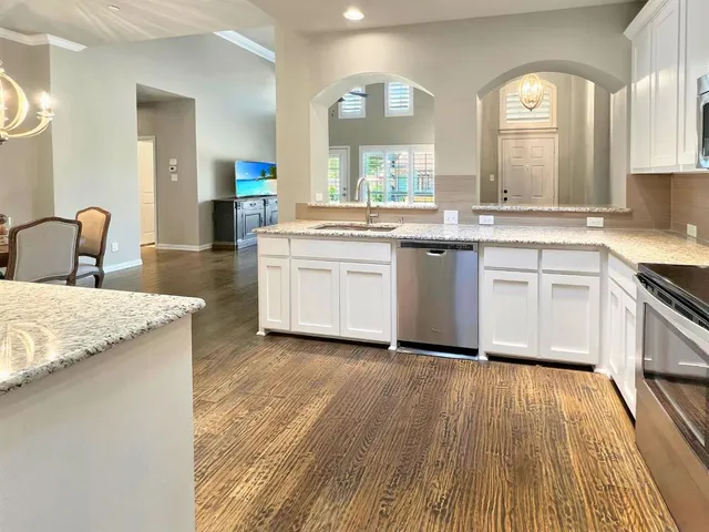 a large kitchen with granite countertop a stove a sink dishwasher and white cabinets with wooden floor