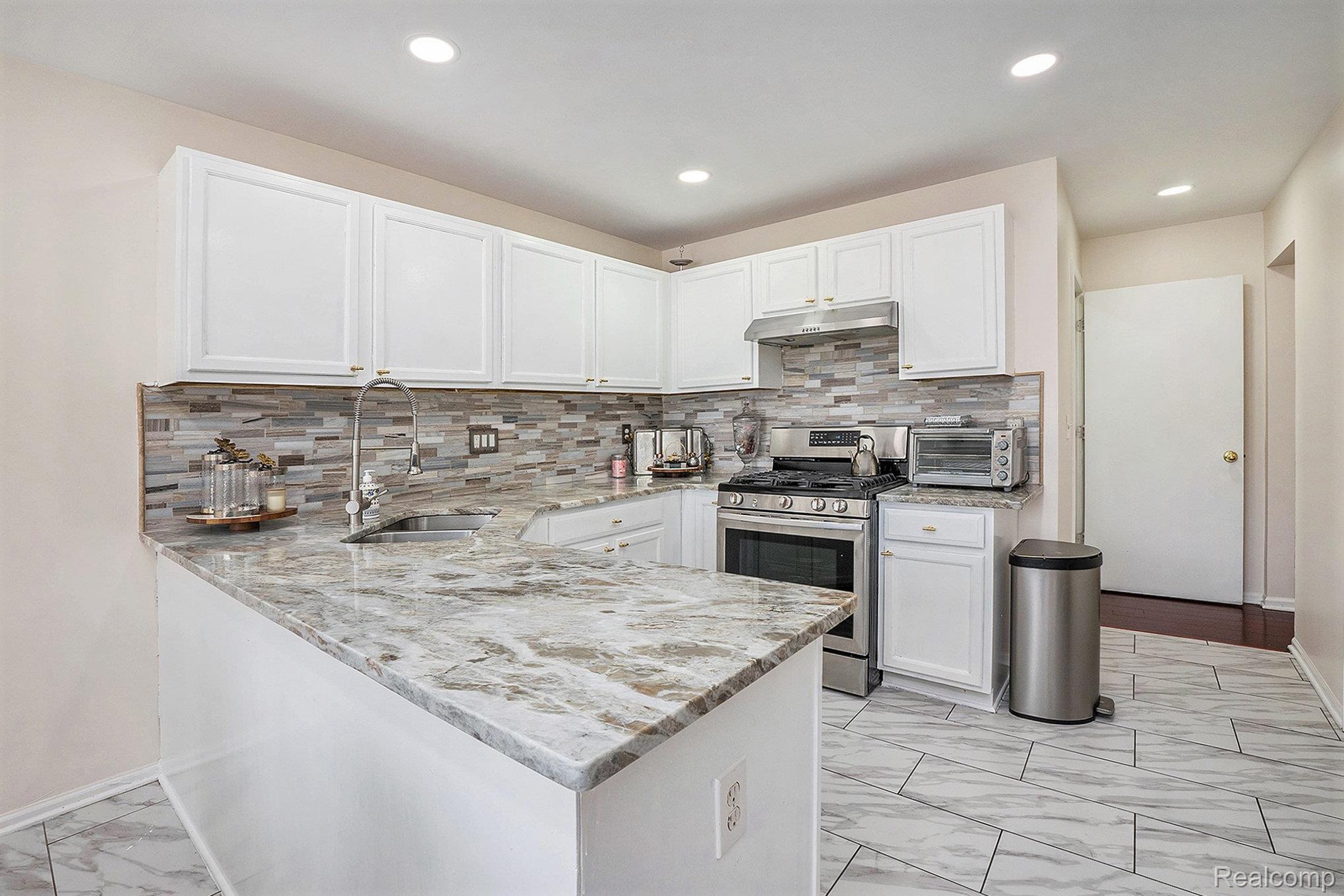 5477 Victory Circle Sterling Heights, MI 48310 - Photo 13 of 32 Well-appointed kitchen featuring white cabinetry, a large kitchen island with a stone-finish countertop, a stainless steel gas range with a matching range hood, and a mosaic tile backsplash