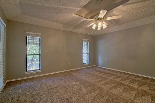 an empty room with chandelier fan and windows