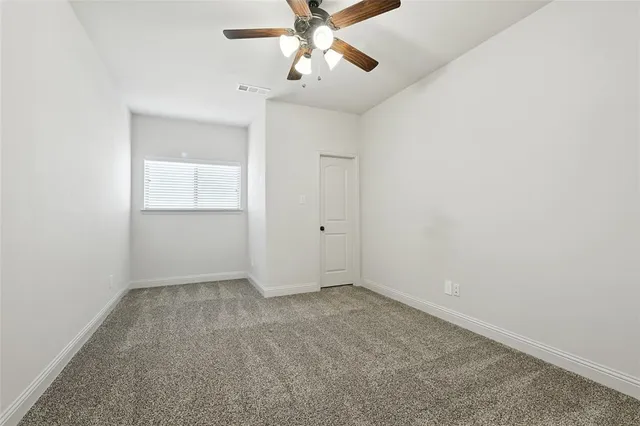 an empty room with chandelier fan and windows