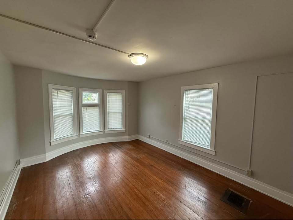 220 College Avenue, Unit 2 DeKalb, IL 60115 - Photo 7 of 14 an empty room with wooden floor and windows