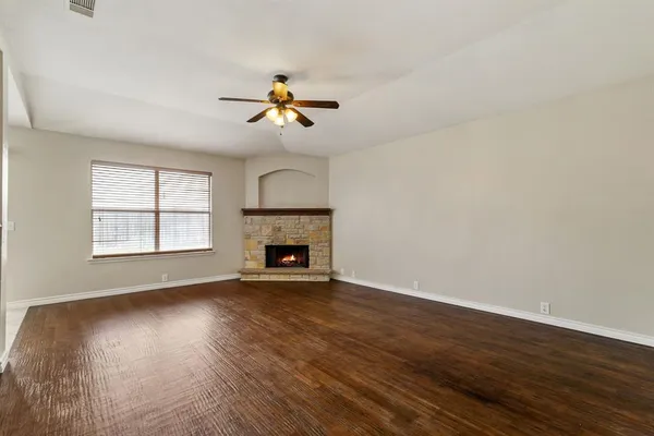 a view of an empty room with wooden floor a fireplace and a window