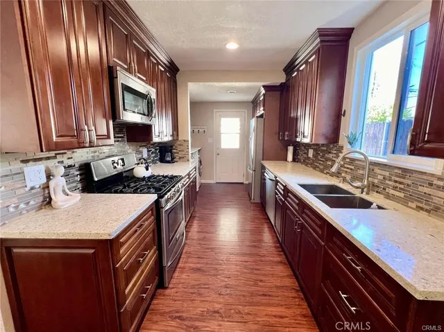 a kitchen with stainless steel appliances granite countertop a stove a sink dishwasher and wooden cabinets with a large window