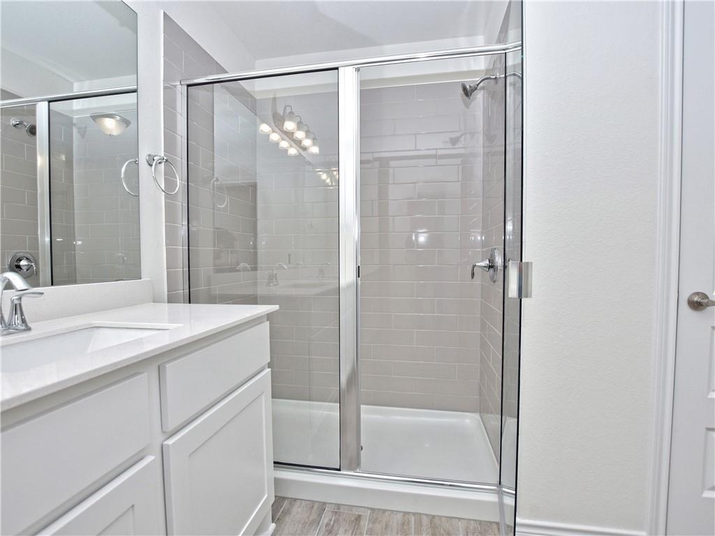 1836 Turtle Bay Loop Leander, TX 78641 - Photo 17 of 32 Bathroom featuring a glass-enclosed shower with subway tile surround, white vanity with integrated sink and chrome faucet, and wood-finish flooring