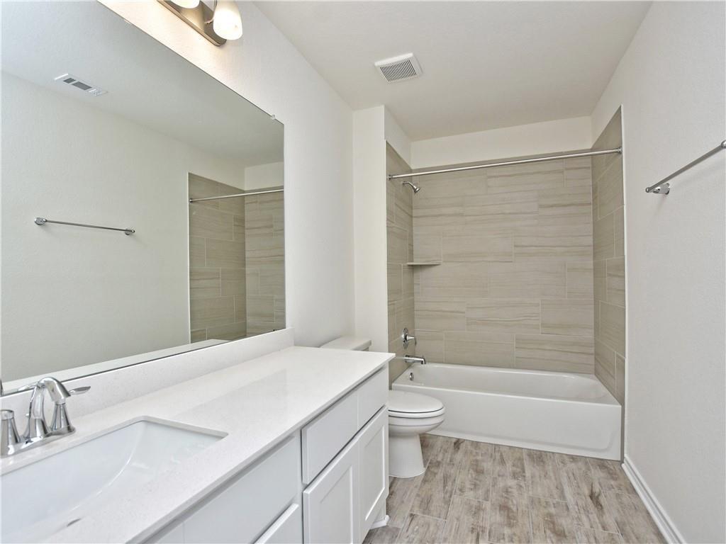 1836 Turtle Bay Loop Leander, TX 78641 - Photo 19 of 32 Bathroom featuring wood-finish flooring, a white vanity with an integrated sink and chrome faucet, a large wall-mounted mirror, and a shower/tub combination with beige horizontal tile surround